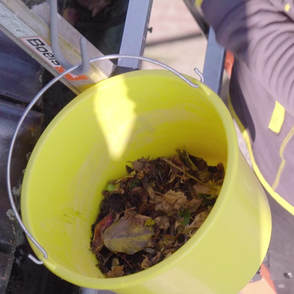 gele praxis emmer met bladeren en vuil dat uit dakgoot komt - praxis pagina voorbereiden op storm