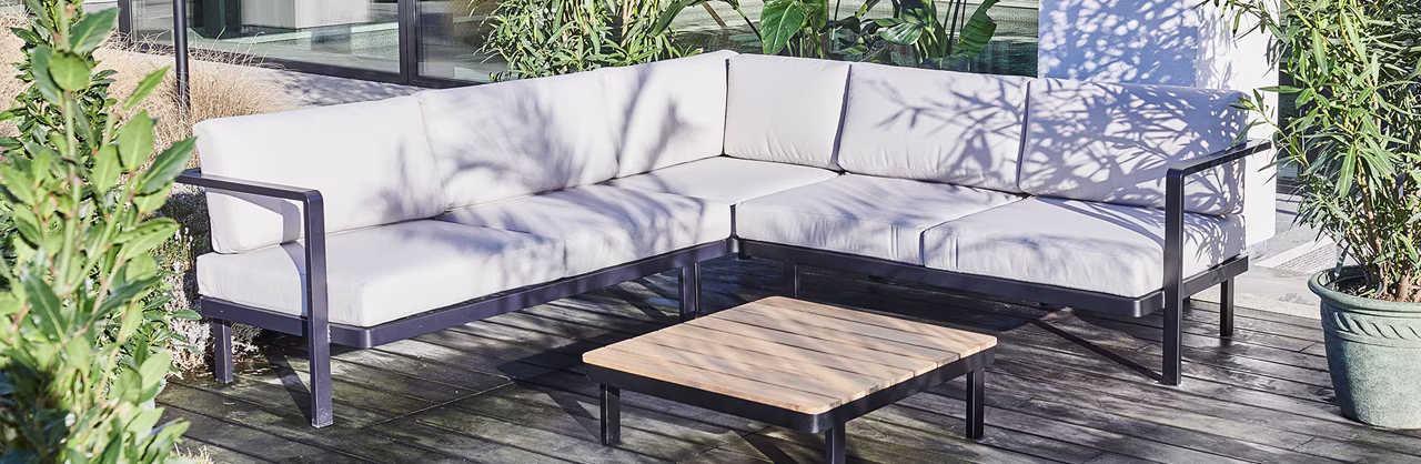 Hoek loungeset met grijze kussens en tafel in tuin 