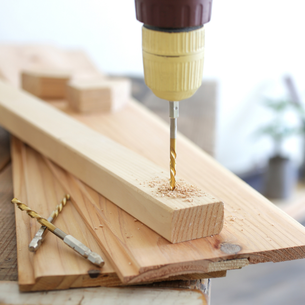 Boormachine die een gat in een houten plank boort, met houtspaanders. | Perceuse perçant un trou dans une planche en bois, avec des copeaux de bois.