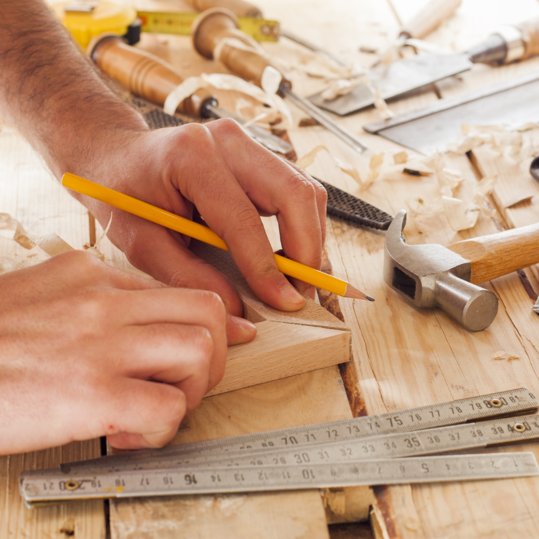 Hand markeert hout met potlood, omringd door hamer en beitel op werkbank | Main marque le bois avec un crayon, entourée d'un marteau et d'un ciseau sur l'établi