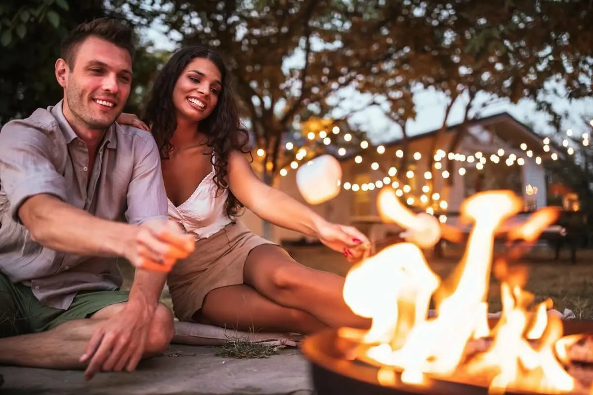 Een man en een vrouw roosteren marshmallows in een kampvuur |  Un homme et une femme font griller des marshmallows dans un feu de camp.