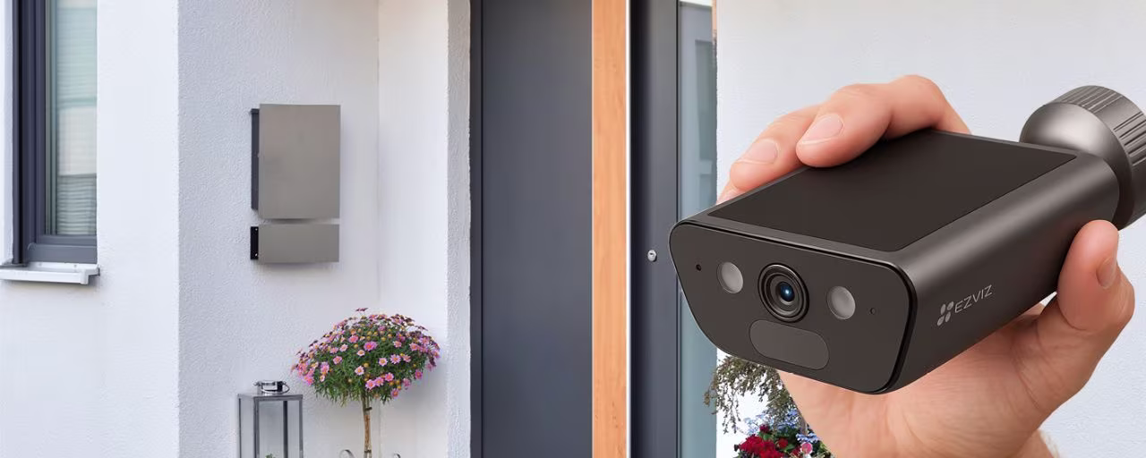 Een persoon met een camera voor een huis | Une personne tenant une caméra devant une maison