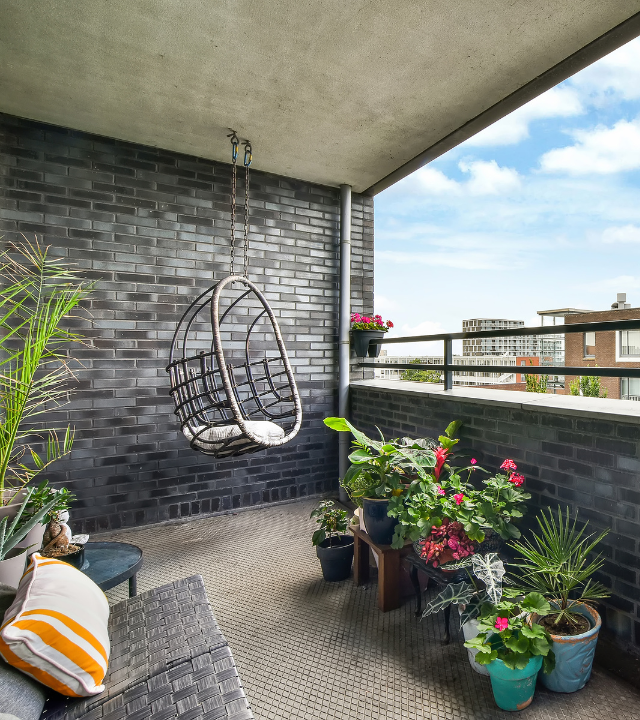 Een grijs balkon met een hangstoel, planten, en zitbank | Un balcon gris avec un fauteuil suspendu, des plantes et un canapé