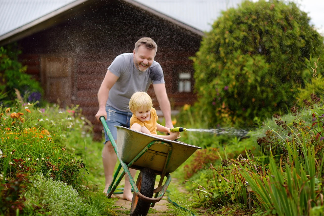 een volwassene en een kind spelen in de tuin in de zomer met een kruiwagen en een slang