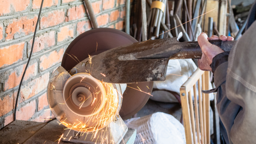 Een man slijpt een botte schop in zijn workshop | Un homme affûte une pelle émoussée dans son atelier