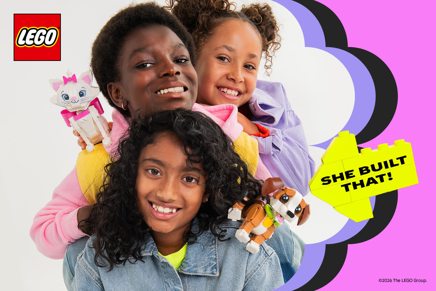 Kolme hymyilevää lasta esittelevät ylpeinä rakentamiaan LEGO-eläinhahmoja värikkäällä taustalla, jossa lukee "SHE BUILT THAT!".