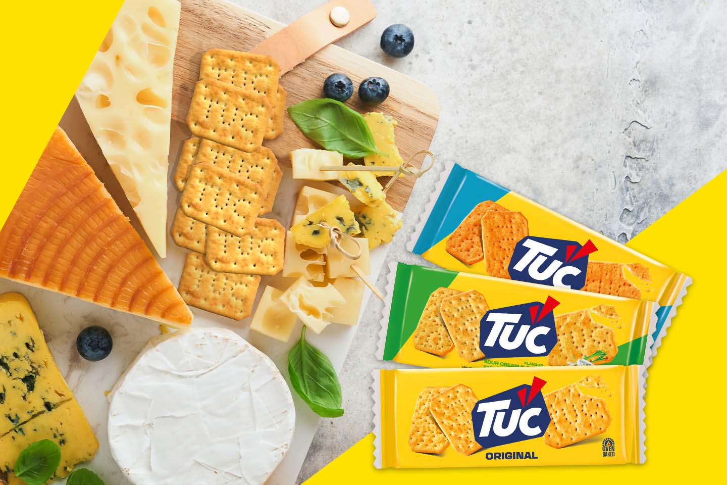 Herkullinen juustolautanen TUC-keksien kanssa, jossa erilaisia juustoja, mustikoita ja basilikanlehtiä puisella tarjoilualustalla.