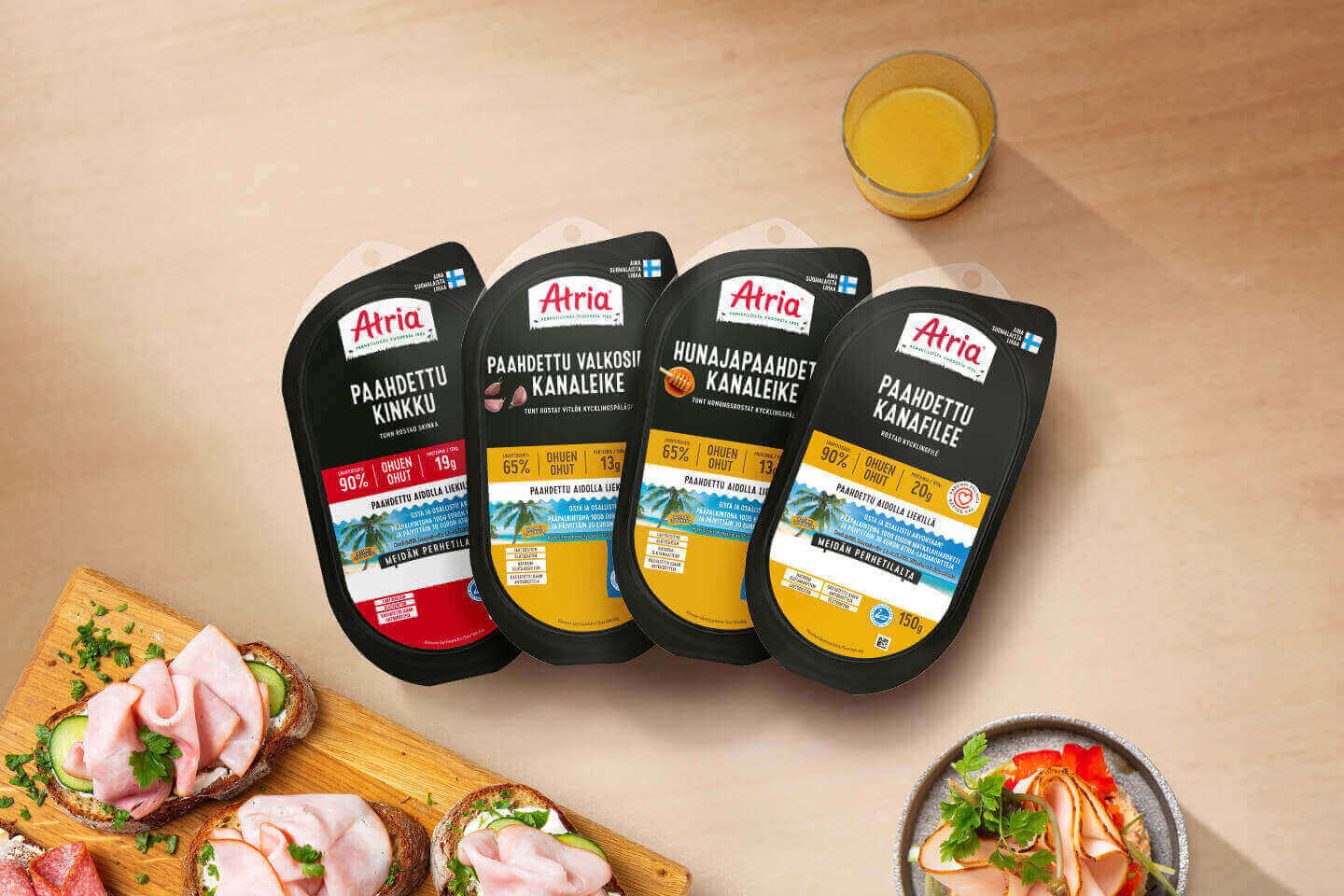Neljä Atrian paahdettu kanatuotetta pöydällä, vieressä voileipiä, mehua ja annoslautanen – maukkaita vaihtoehtoja arkeen.