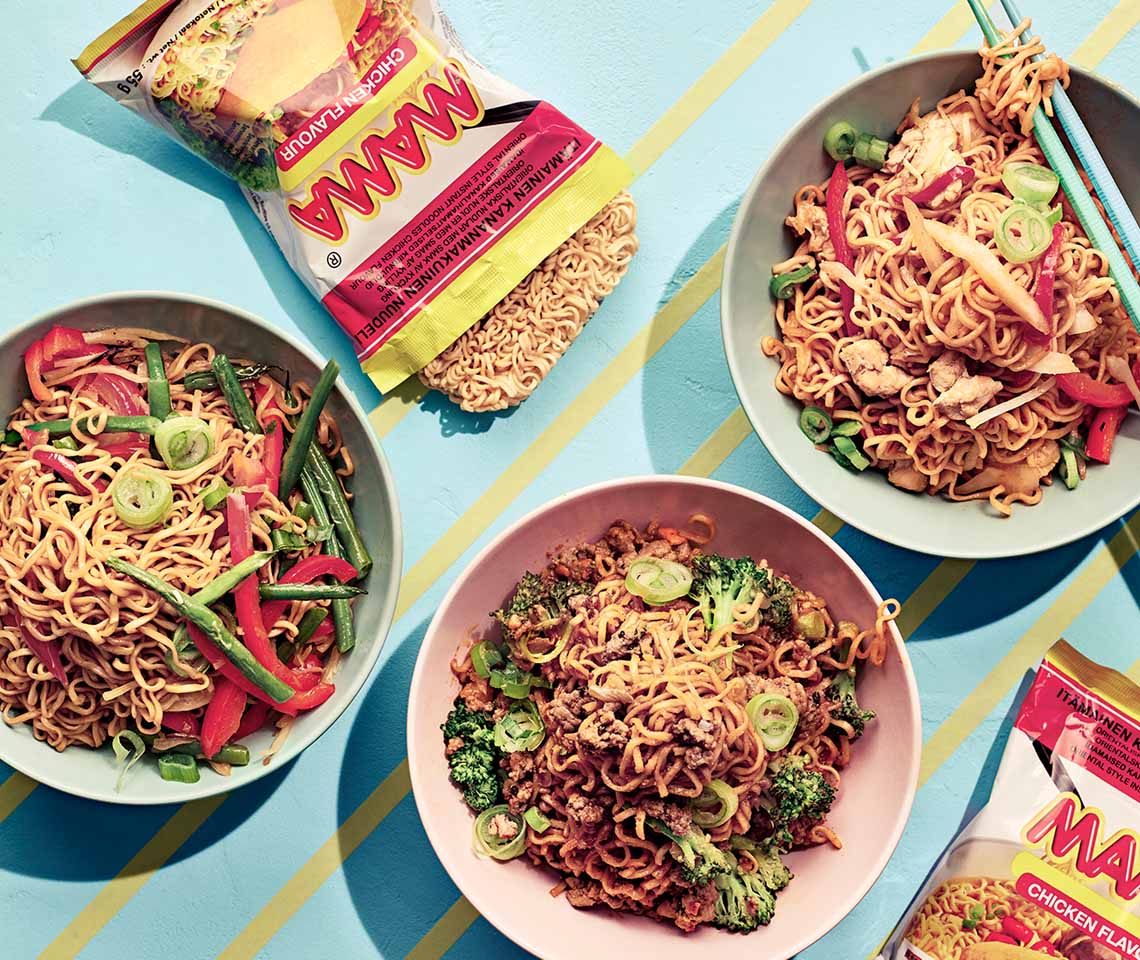 Kolme kulhoa herkullisia nuudeliannoksia vihanneksilla ja pakkaus Mama-nuudeleita sinisellä pöydällä.