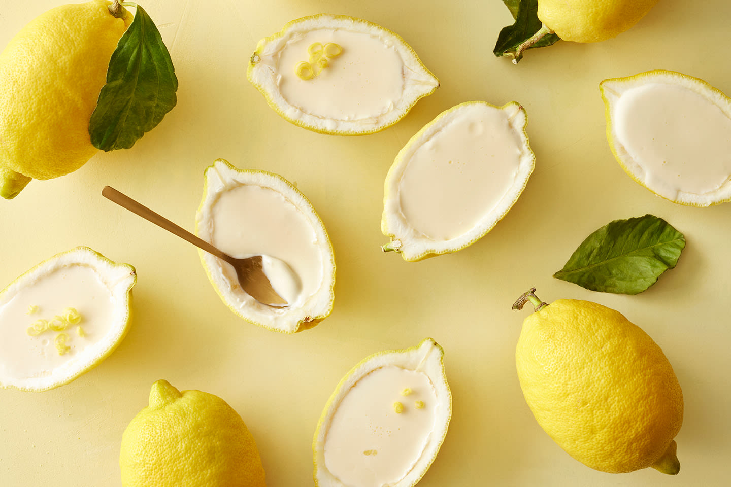 Raikkaita sitruunapuoliskoja täytetty kermaisen valkoisella täytteellä keltaisella taustalla, yksi lusikalla nautittavana.