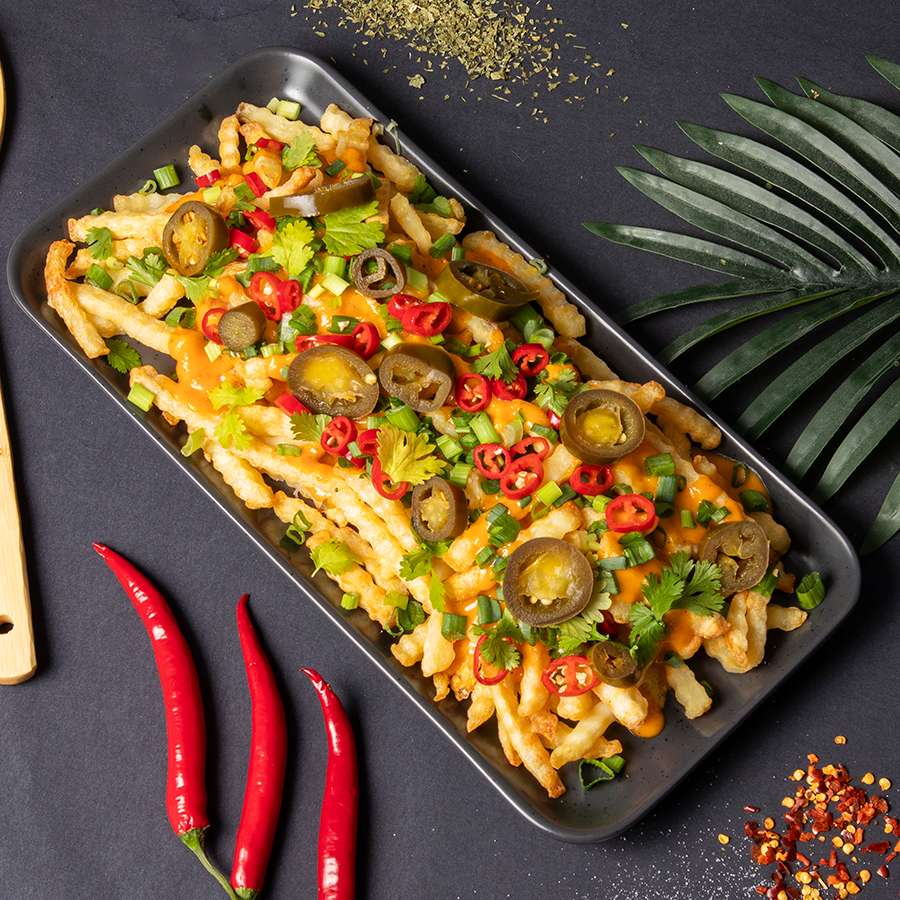 Tarjoilualustalla ranskalasia, joiden päällä kastiketta, jalapenoja, chiliä ja korianteria.