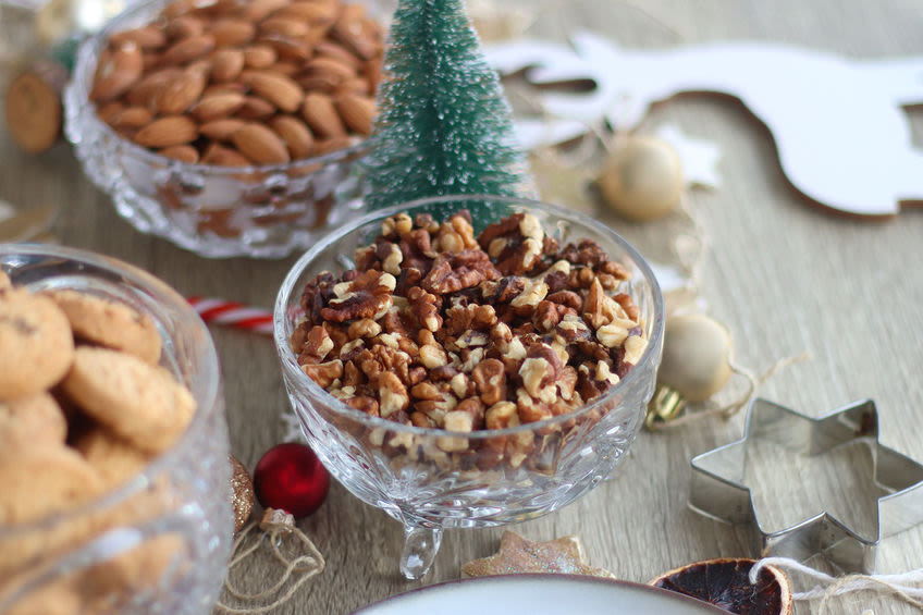 Jouluinen pöytä täynnä pähkinöitä kristallikulhoissa, pieni joulukuusi keskellä ja piparkakkumuotteja ympärillä.