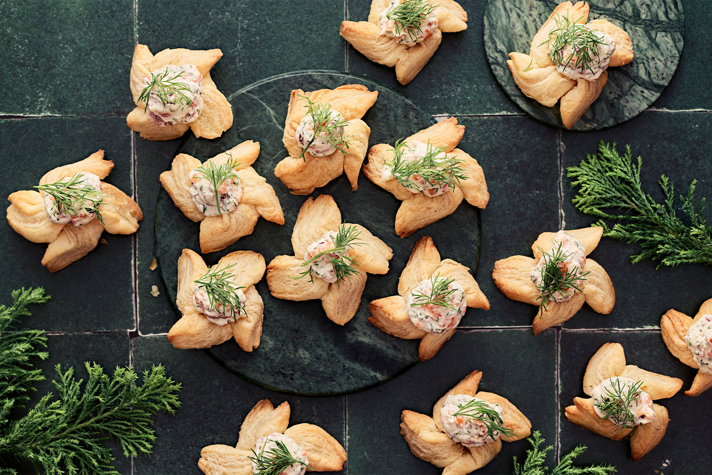 Kullanvärisiä voitaikinaleivoksia täytettynä herkullisella kalatäytteellä ja koristeltuna tuoreella tillillä tummalla kivialustalla.