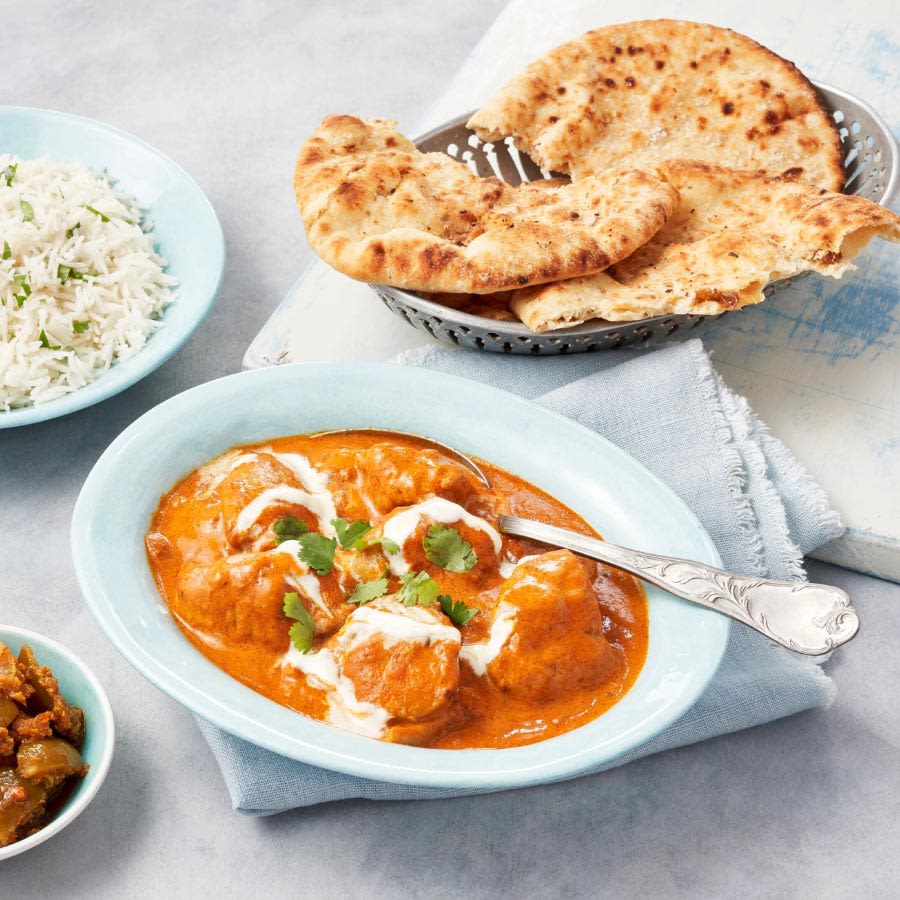 Vaaleansinisellä lautasella tarjoiltu butter chicken -curry, jonka vieressä lisukkeena riisiä ja naan-leipää.