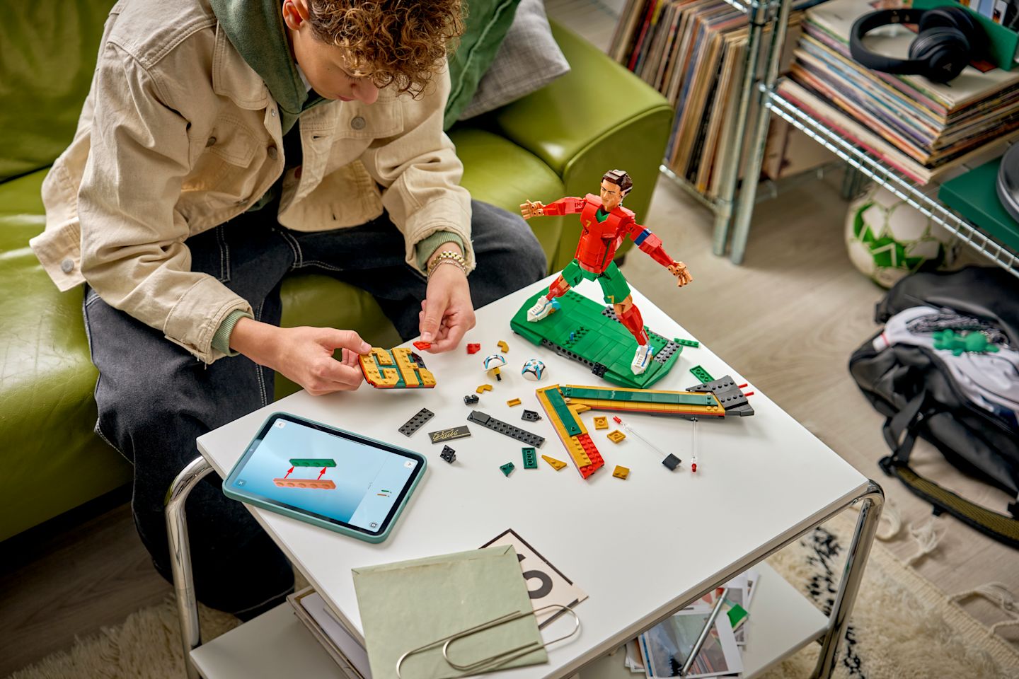 Nuori henkilö kokoaa LEGO-jalkapalloilijahahmoa pöydällä tabletin ohjeiden avulla viihtyisässä huoneessa.