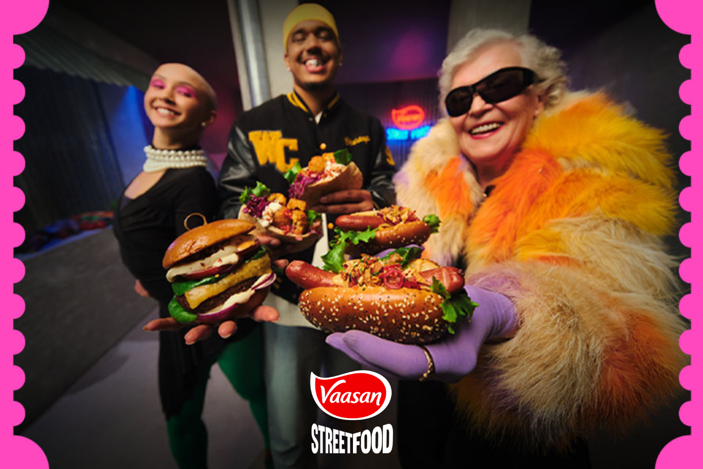 Kolme iloista henkilöä esittelee hampurilaisia ja hot dogeja pinkillä kehystetyssä kuvassa, Vaasan Street Food -logo