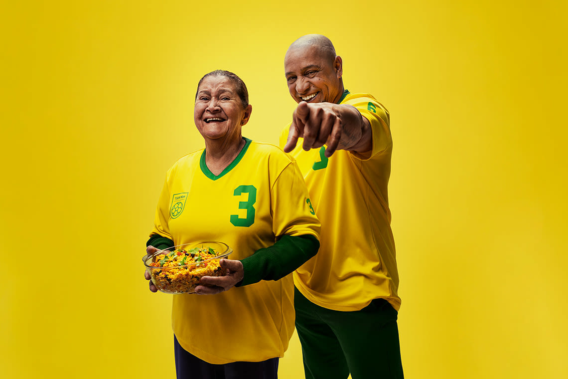 Jalkapalloilija Roberto Carlos äitinsä kanssa keltavihreissä paidoissa keltaisen taustan edessä. Äidillä on kulhollinen salaattia kädessään.