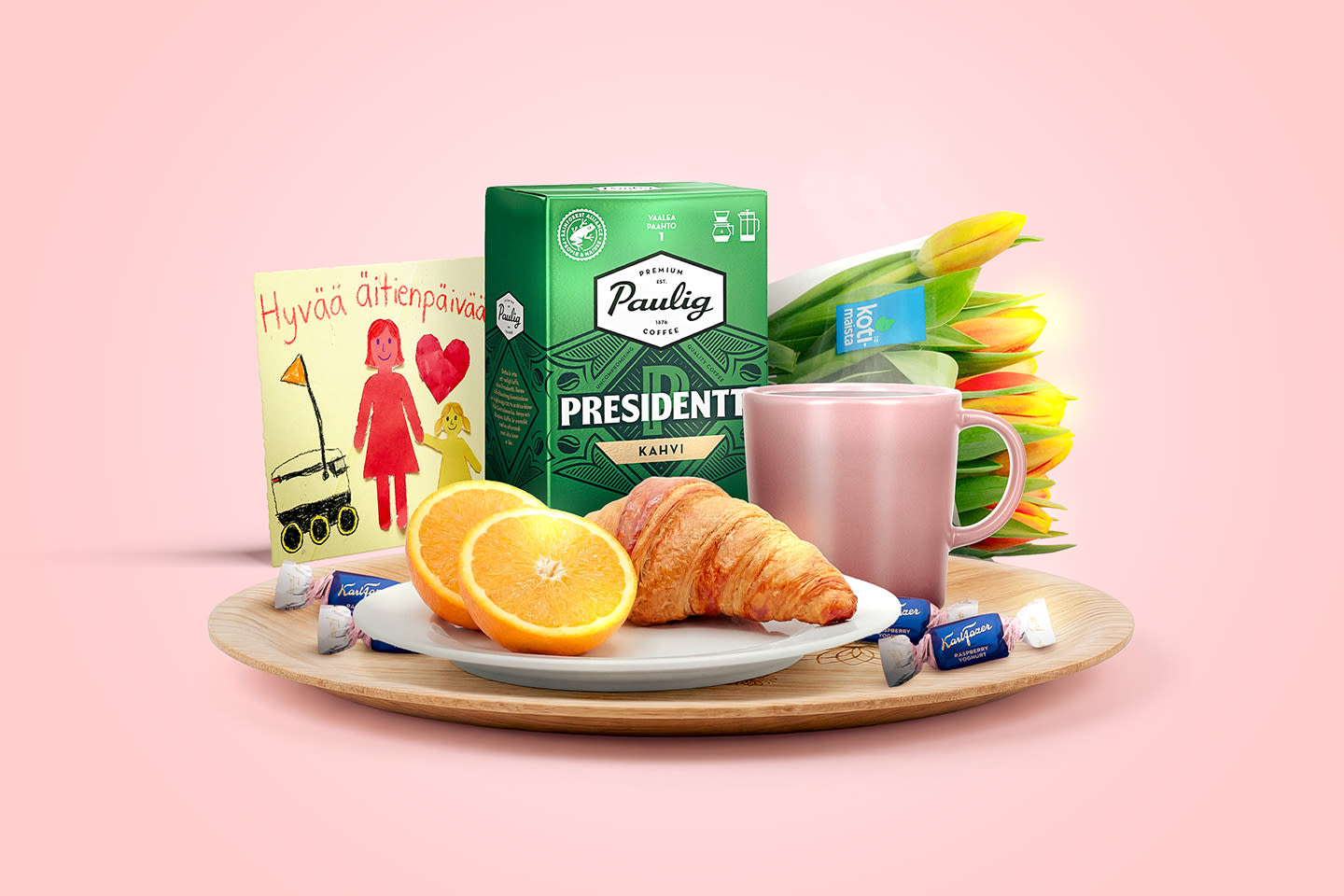 Viihtyisä äitienpäivän aamiaiskattaus puualustalla: croissant, appelsiineja, kahvia, kortti ja keltaisia tulppaaneja vaaleanpunaisella taustalla.