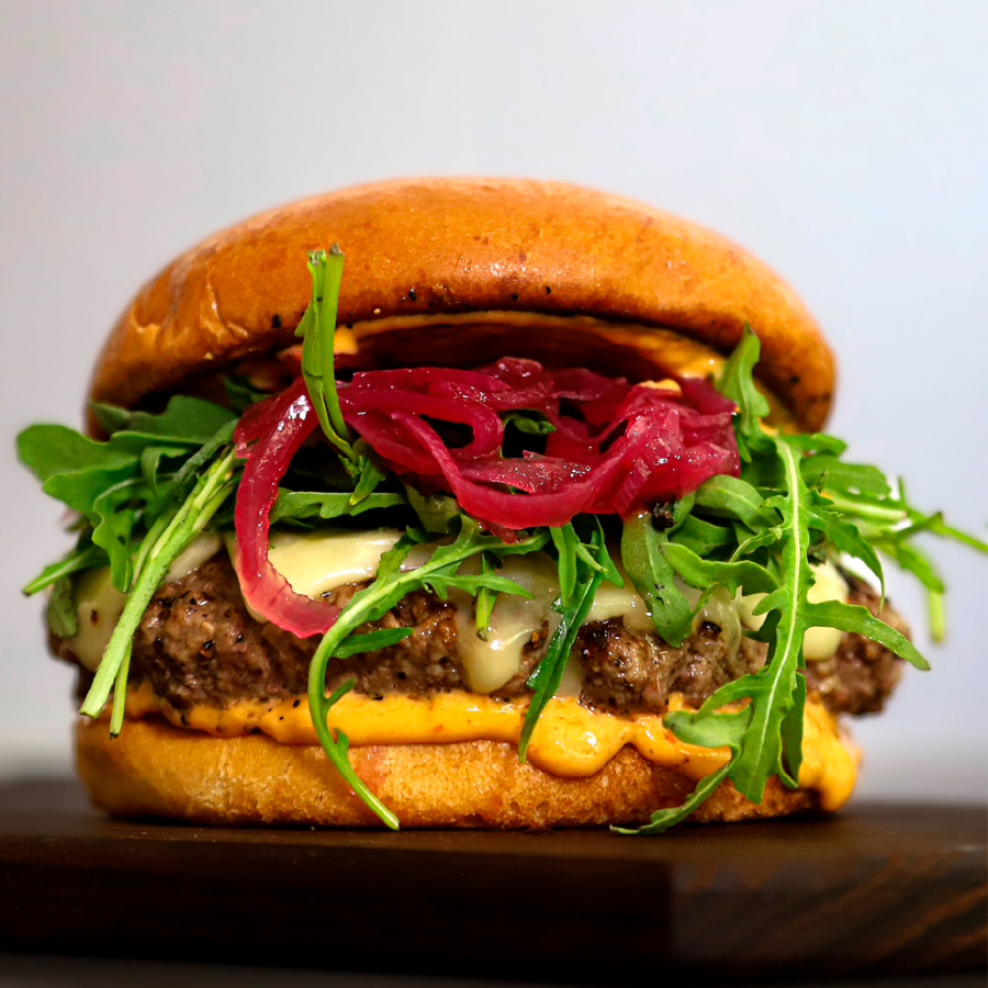 Mehevä hampurilainen rapealla sämpylällä, pihvillä, juustolla, tuoreella rucolalla ja punasipulilla.