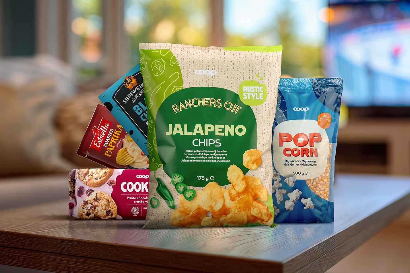 Pöydällä on useita herkkupakkauksia: jalapeño-sipsejä, popcornia, keksejä ja paprikachipsejä.