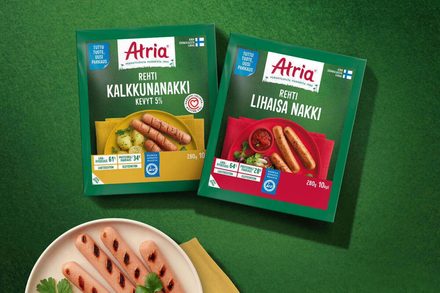 Atrian kalkkunanakki ja lihaisa nakki -pakkaukset vihreällä taustalla, lautasella grillattuja nakkeja.
