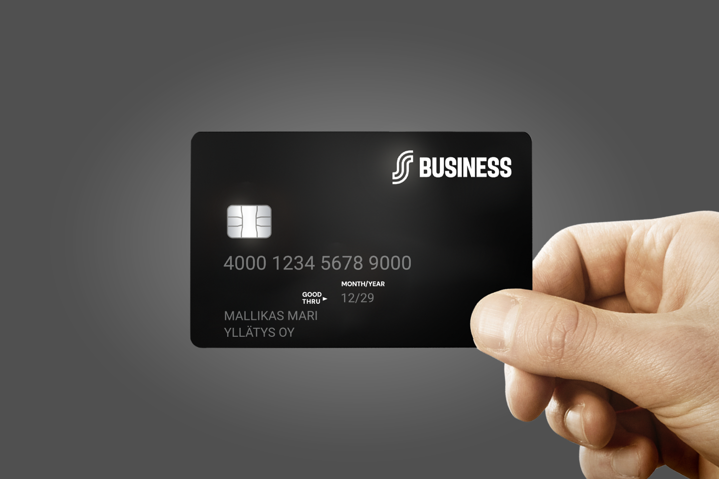 Käsi pitää mustaa Business-maksukorttia, jossa näkyy sirun, korttinumeron ja voimassaoloajan lisäksi kortinhaltijan nimi.