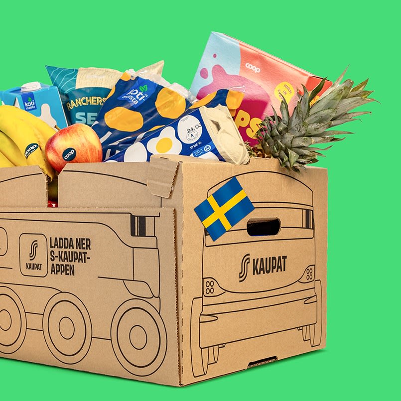 S-kaupat-logolla varustettu pahvilaatikko täynnä ruokaostoksia, kuten banaaneja, ananasta ja pakattuja tuotteita, vihreällä taustalla. Laatikossa on Ruotsin lipun kuva.