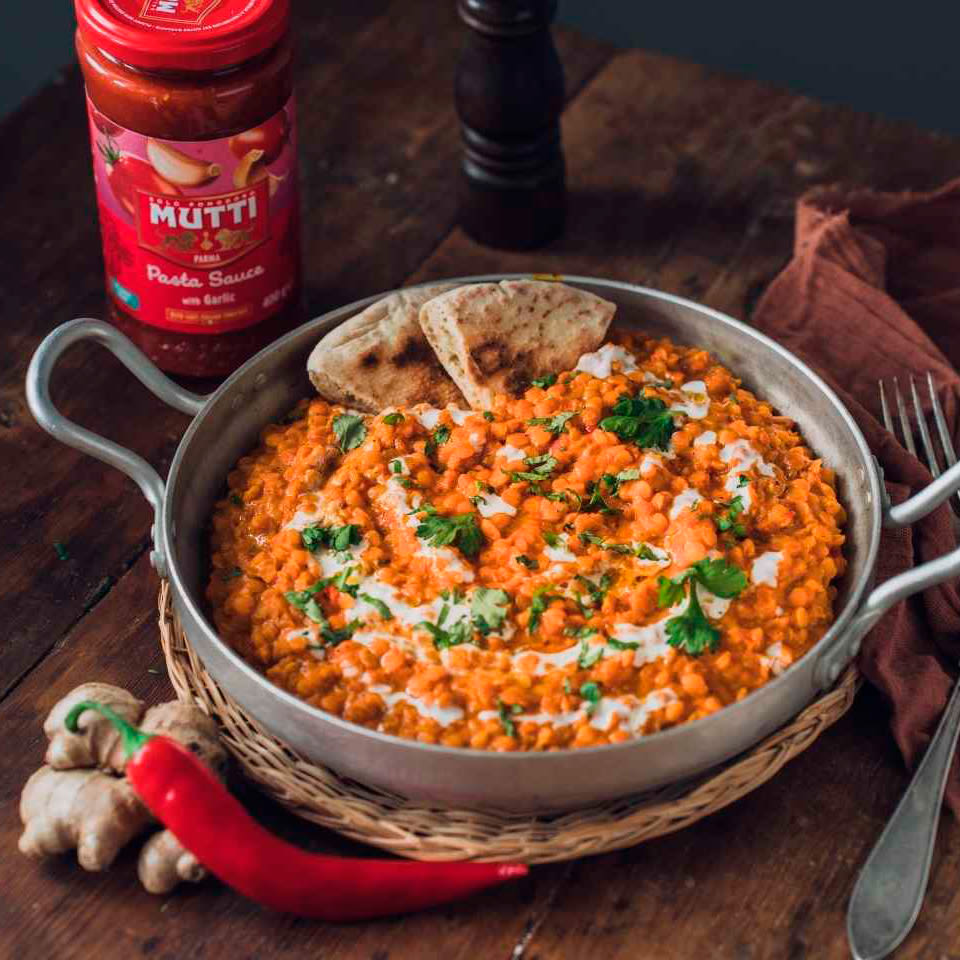 Pannussa oranssia linssimuhennosta korianterin ja kookosmaidon kera, vieressä Mutti-tomaattikastike, inkivääri ja punainen chili.