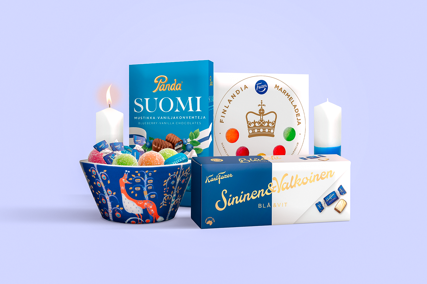 Suomalaisia makeislahjoja sinisävyisellä taustalla: Fazerin suklaata, marmeladeja koristeellisessa kulhossa ja kaksi kynttilää.