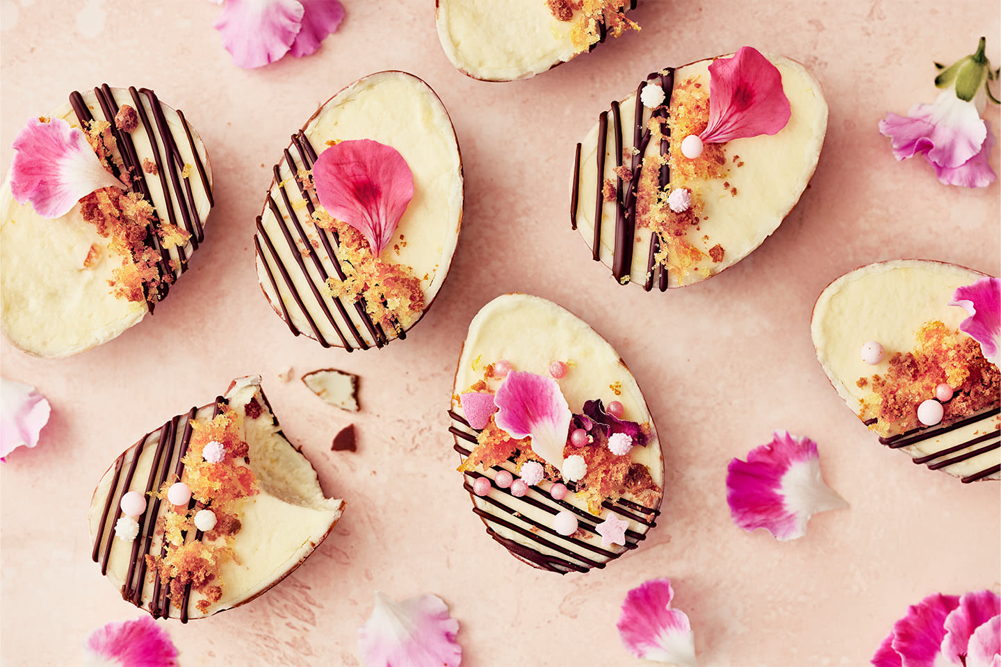 Pieniä marenkipesiä koristeltu värikkäillä suklaamunilla ja kinuskilla, ympärillä keväisiä kukkia ja oksia vaaleanvihreällä taustalla.