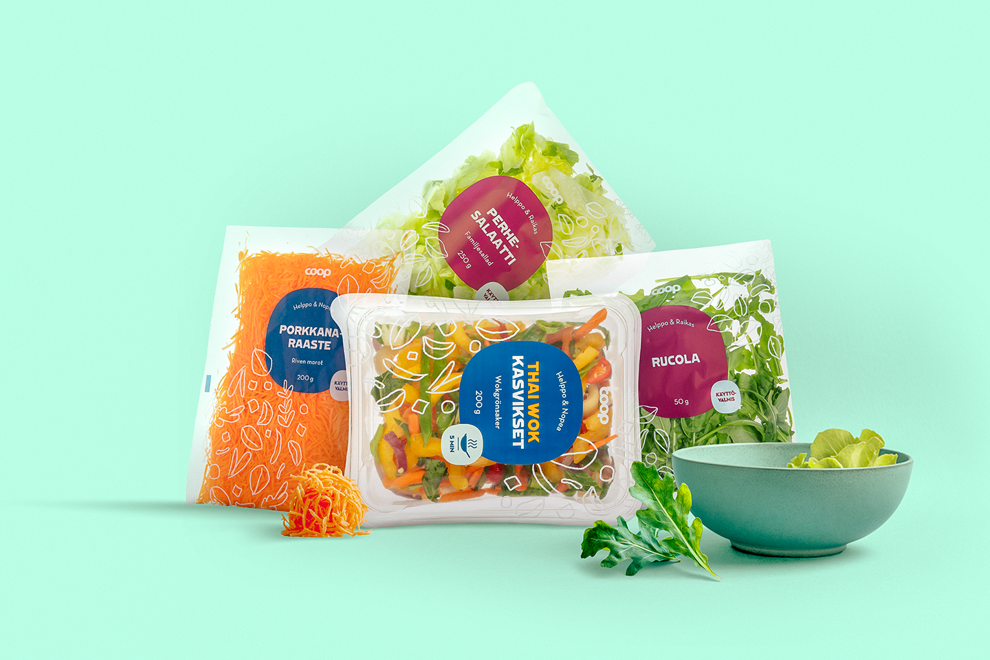 Raikkaita salaattiaineksia pakattuina pusseissa: porkkanaraastetta, thaimaalaista kasvisekoitusta, rucolaa ja perhe-salaattia vihreällä taustalla.