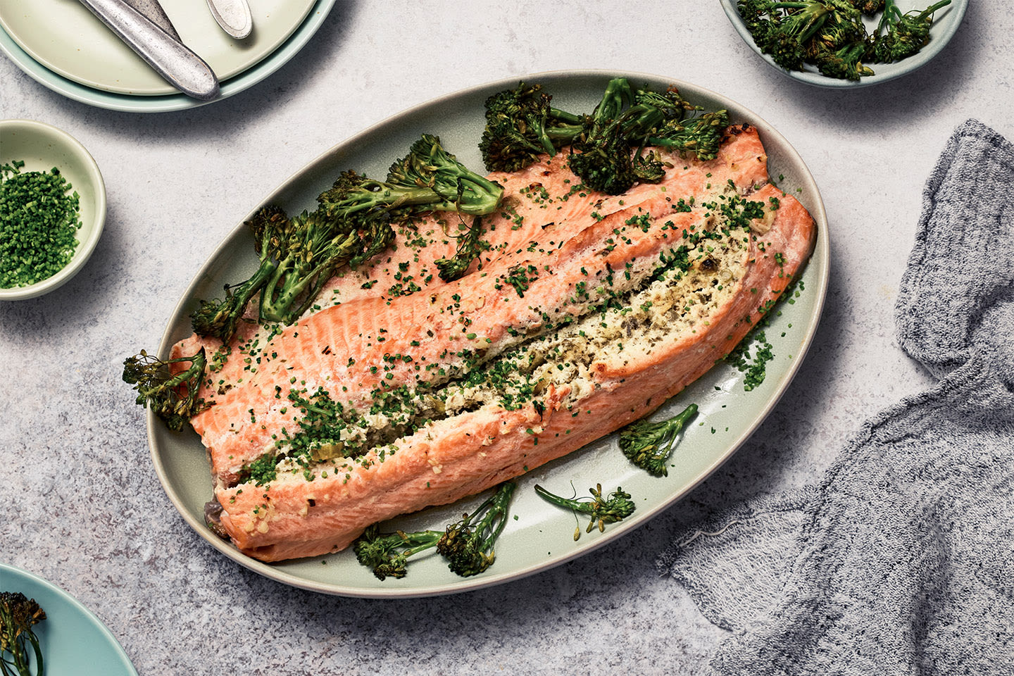 Mehevä lohifilee vaaleanvihreällä lautasella, koristeltuna paahdetulla parsakaalilla ja yrteillä.