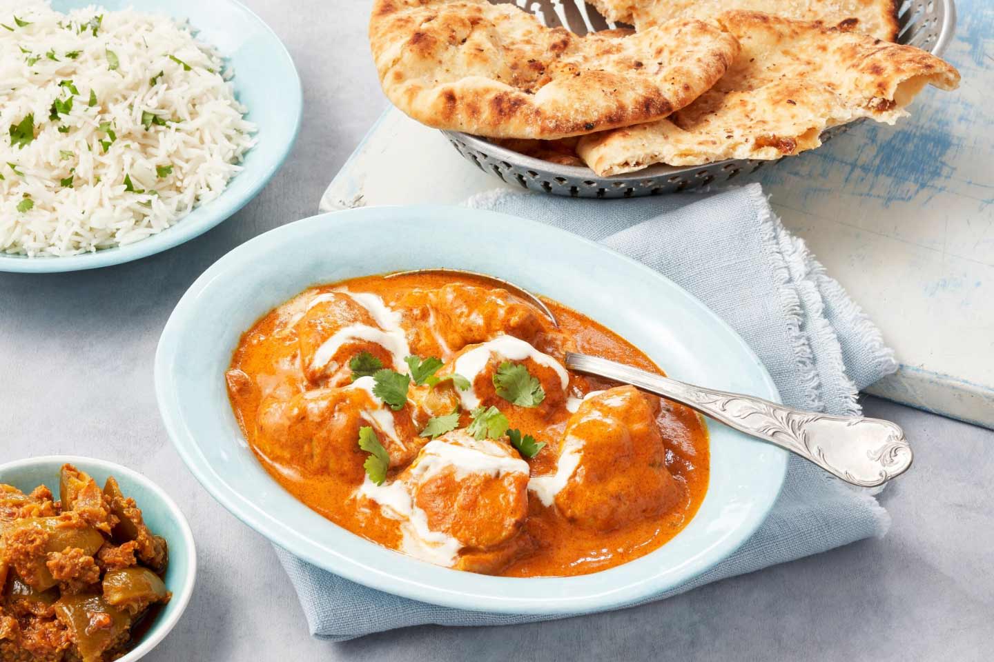 Vaaleansinisellä lautasella tarjoiltu butter chicken -curry, jonka vieressä lisukkeena riisiä ja naan-leipää.