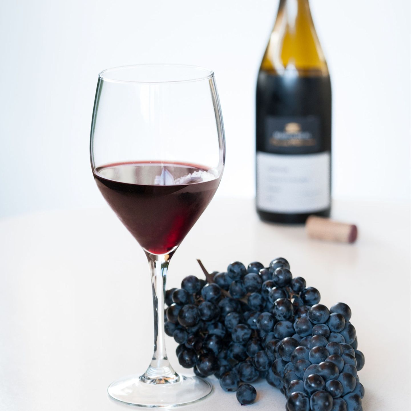 Punaviinilasillinen taustalla olevan avautun pullon ja viinirypäleiden kanssa