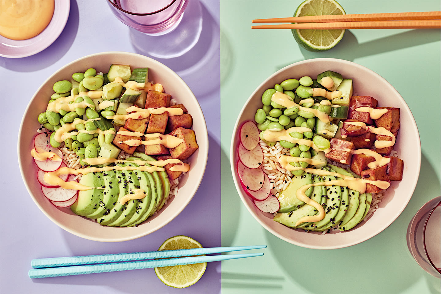 Kaksi värikästä poke-kulhoa täynnä tofua, avokadoa, edamamea ja riisiä, koristeltuna kastikkeella ja syöpuikoilla.