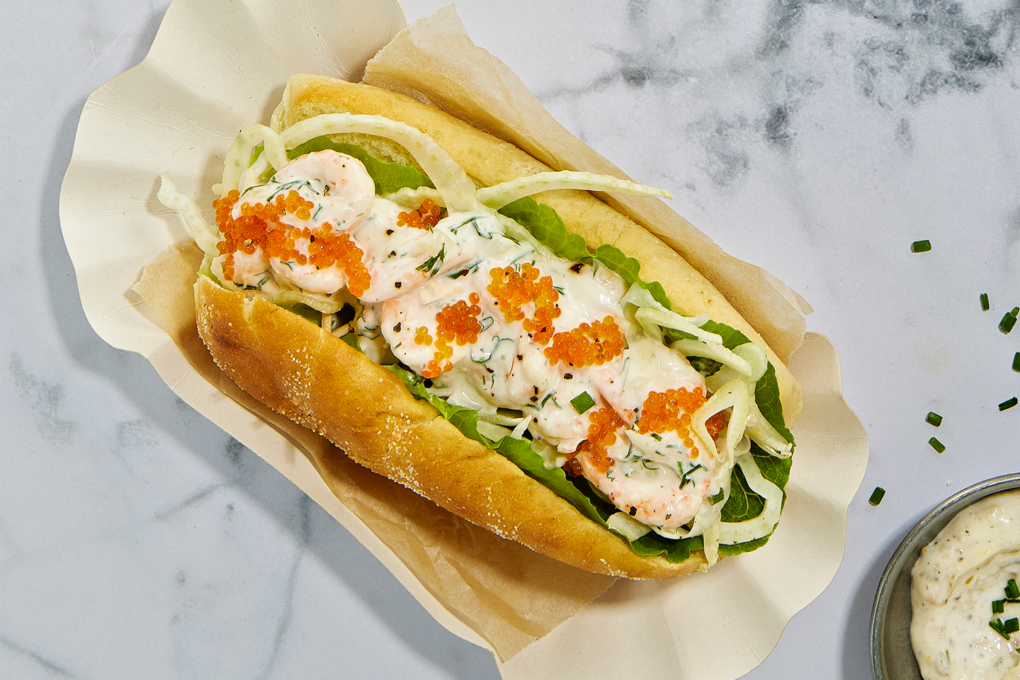 Katkarapuhotdog, täytteenä salaattia, kurkkua, majoneesia ja oranssia mätiä, aseteltuna paperille.
