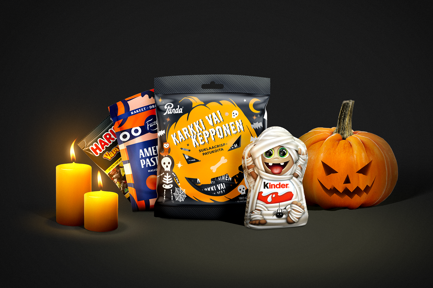 Karkkipusseja ja Kinder-suklaata mustalla taustalla. Vieressä kaksi oranssia kynttilää ja kurpitsa Halloween-kaiverruksilla.