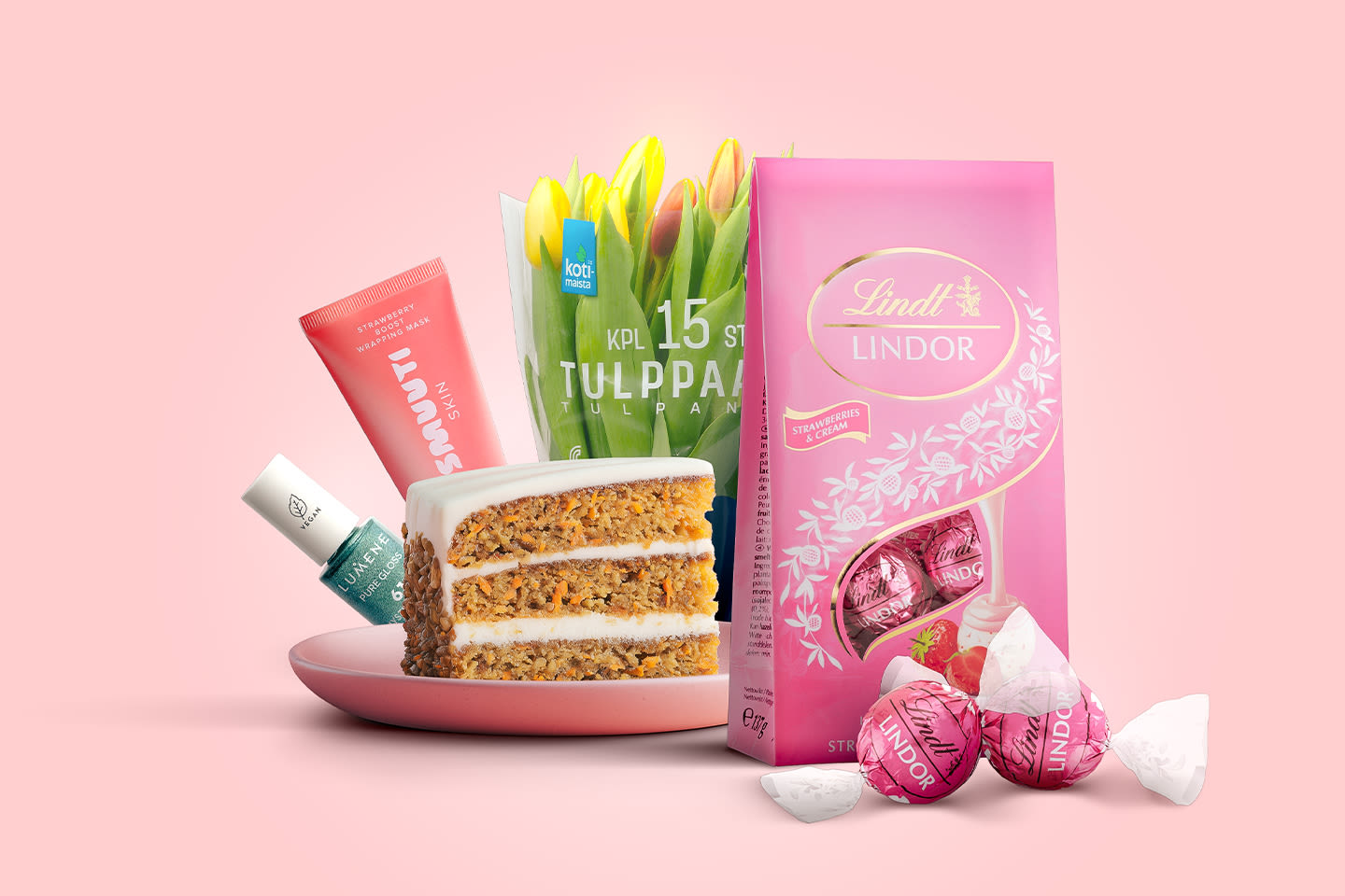 Keväinen hemmotteluhetki: porkkanakakkua, keltaisia tulppaaneja, Lindt-suklaata ja ihonhoitotuotteita vaaleanpunaisella taustalla.