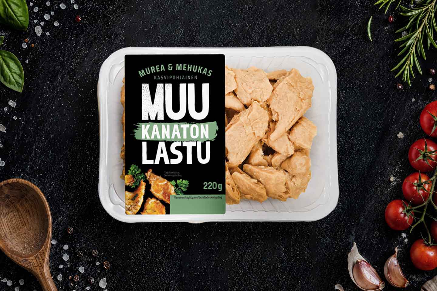 Kasvipohjainen Muu Kanaton Lastu -tuote 220 gramman pakkauksessa, ympärillä tuoreita yrttejä, tomaatteja ja valkosipulia.