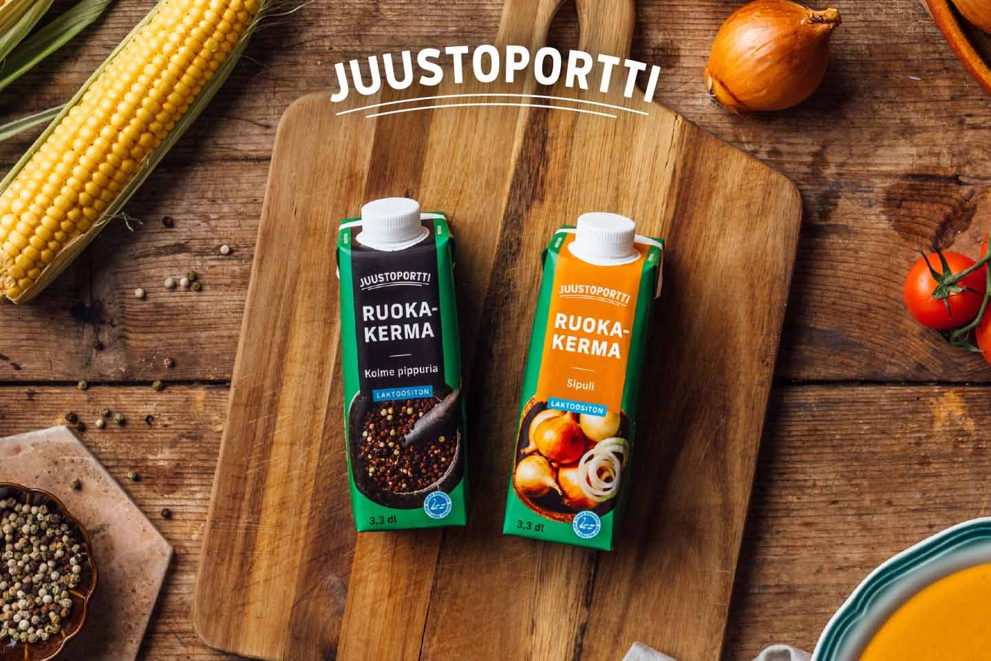 Juustoportin ruokakermapakkaukset puisella leikkuulaudalla, ympärillä tuoreita raaka-aineita kuten maissia, sipulia ja tomaattia.