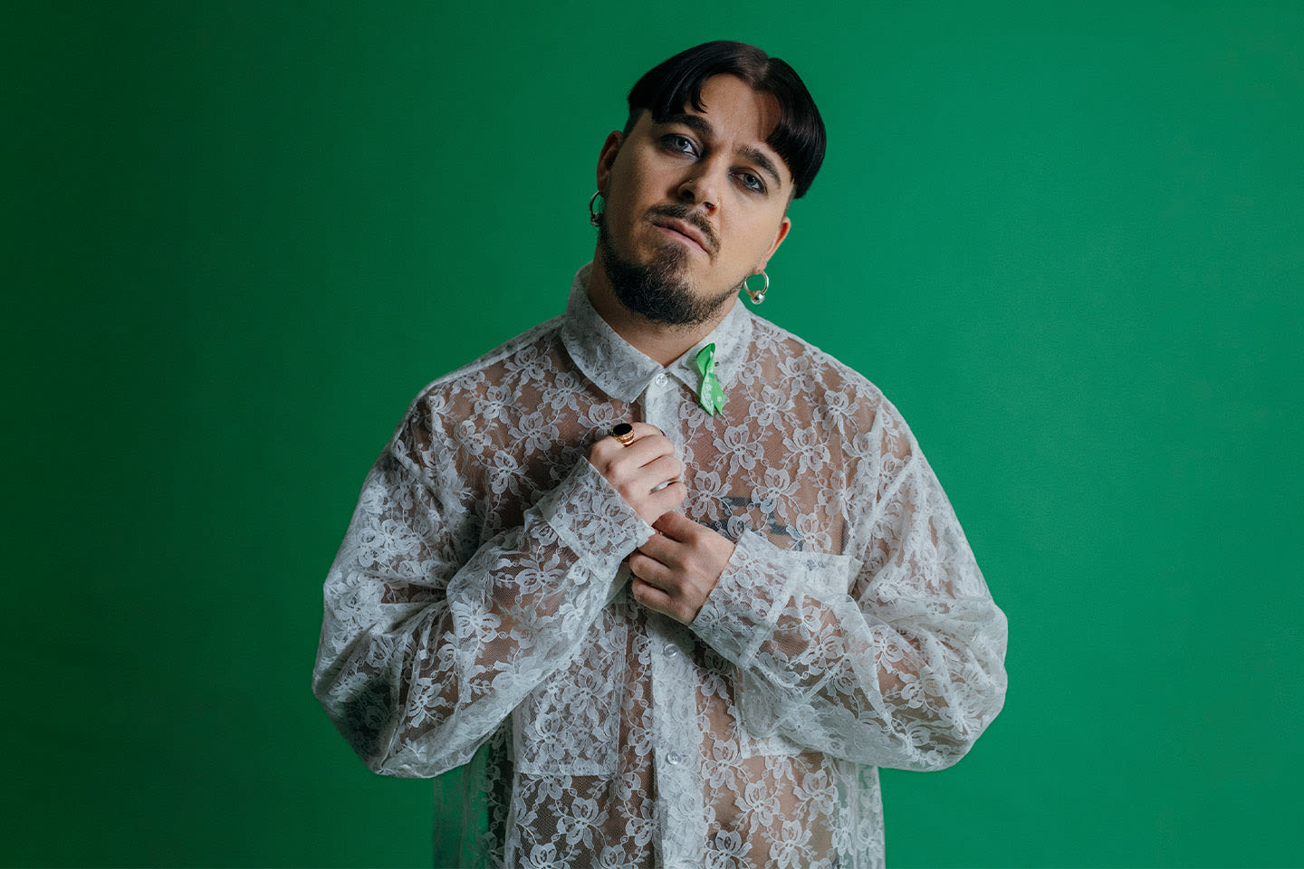 Käärijä vihreää taustaa vasten pukeutuneena tyylikkääseen valkoiseen pitsipaitaan, mielinauhaan ja korvakoruihin.