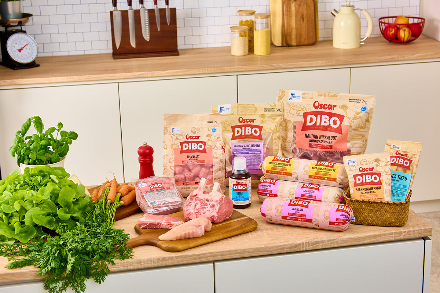 Oscar DIBO -tuotevalikoima keittiötasolla tuoreiden vihannesten ja lihan kanssa, taustalla vaalea keittiö koristeellisine yksityiskohtineen.