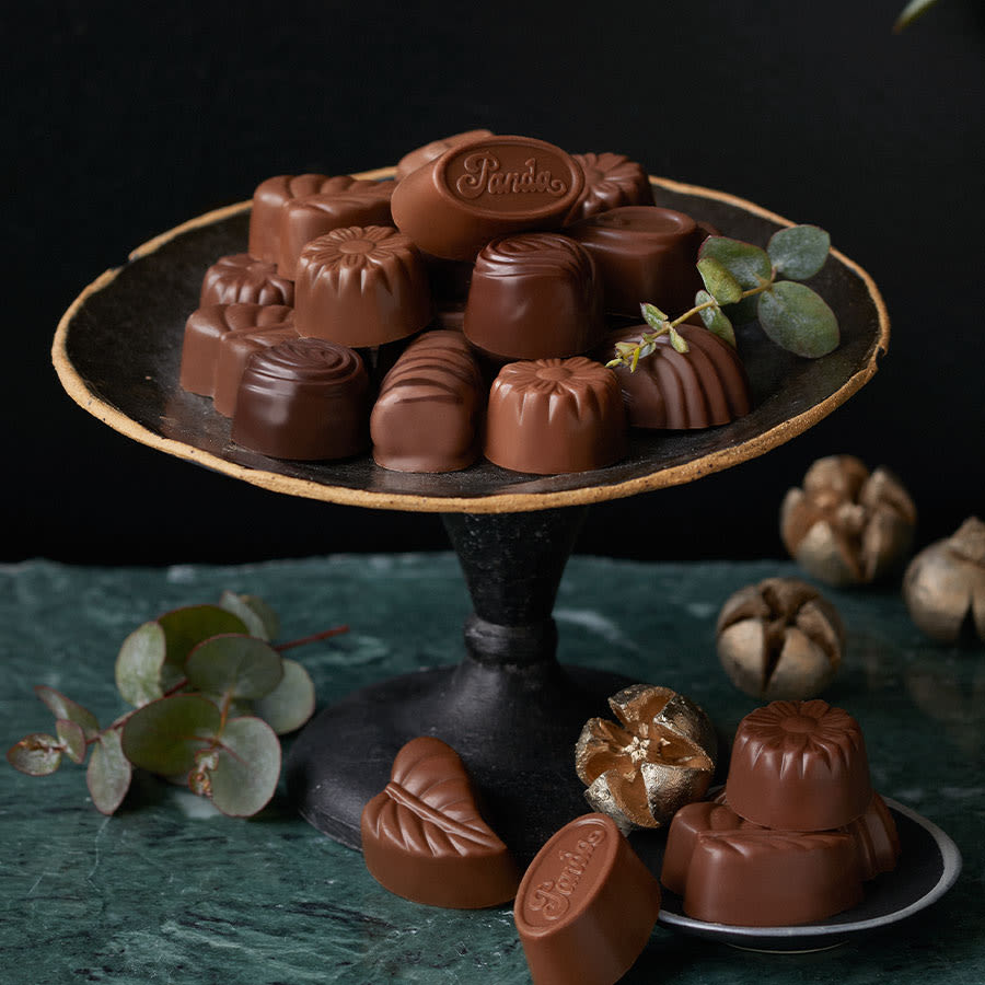 Herkullisia Pandan suklaakonvehteja kauniisti esillä mustalla kultareunaisella tarjoiluvadilla, koristeltuna eukalyptuksen oksilla.