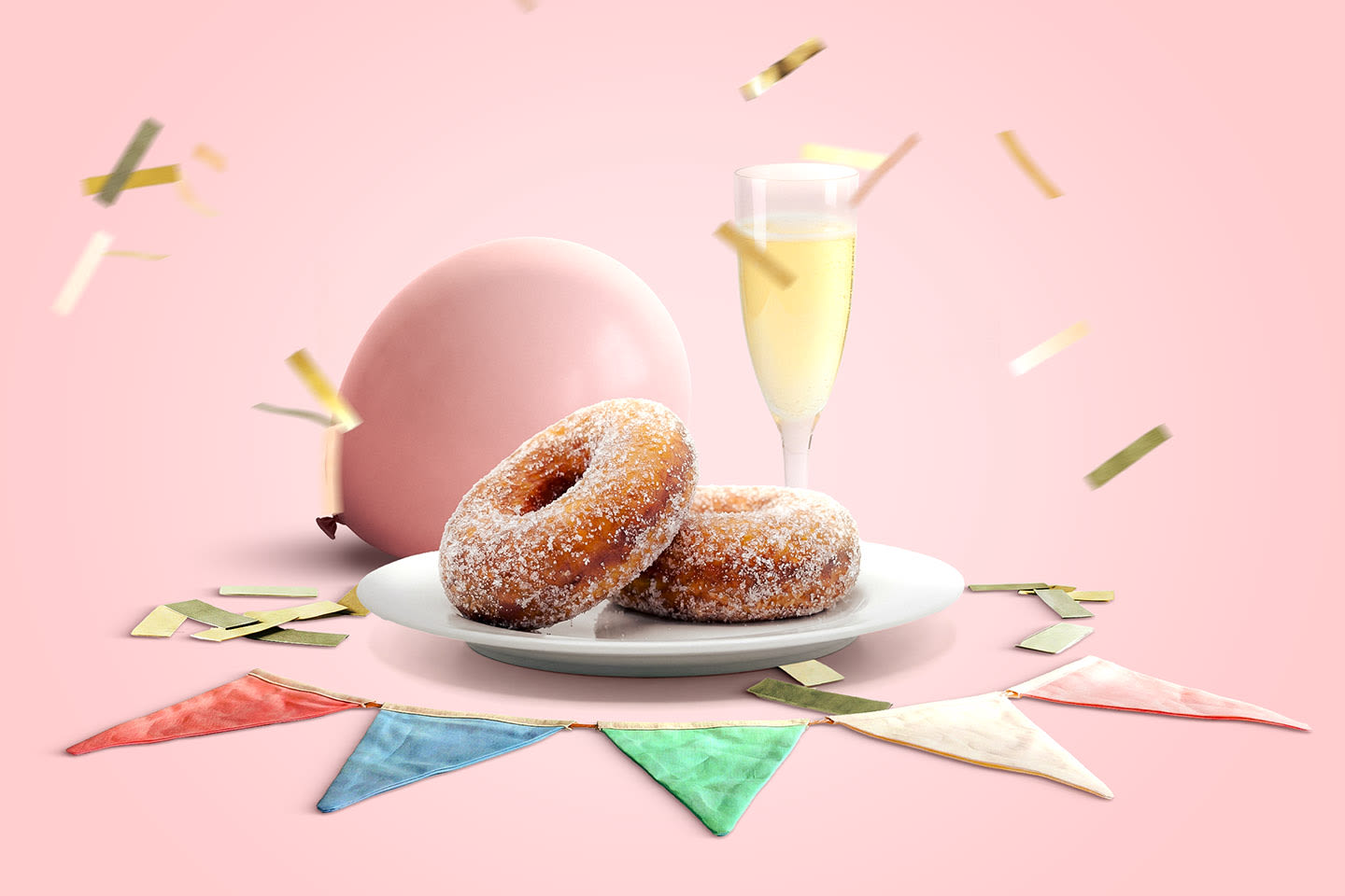 Sokeroidut munkit lautasella, samppanjalasi ja vaaleanpunainen ilmapallo juhlavassa asetelmassa värikkäiden viirien ja kultaisten konfettien keskellä.