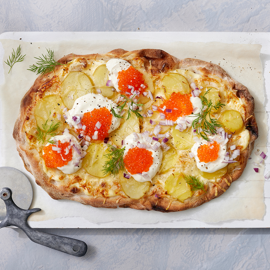 Perunapinsa, jossa päällä ranskankermaa, mätiä, silputtua punasipulia ja tuoretta tilliä, leivinpaperin päällä.