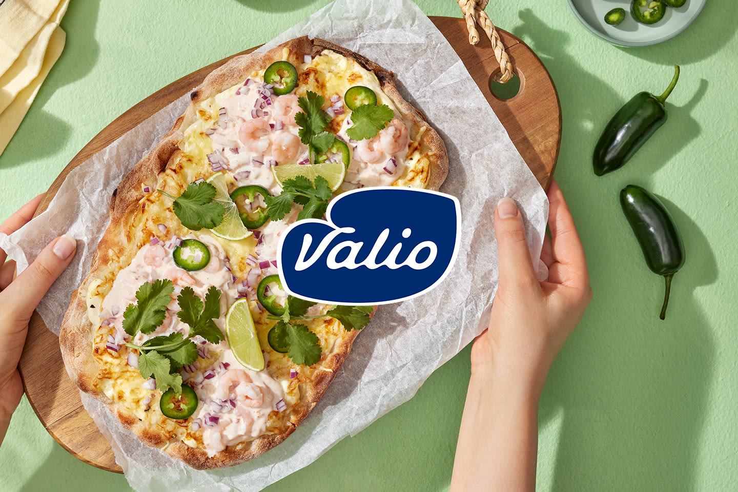Pinsa katkaravuilla, jalapenoviipaleilla, korianterilla ja limetillä puisella leikkuulaudalla, Valio-logo.