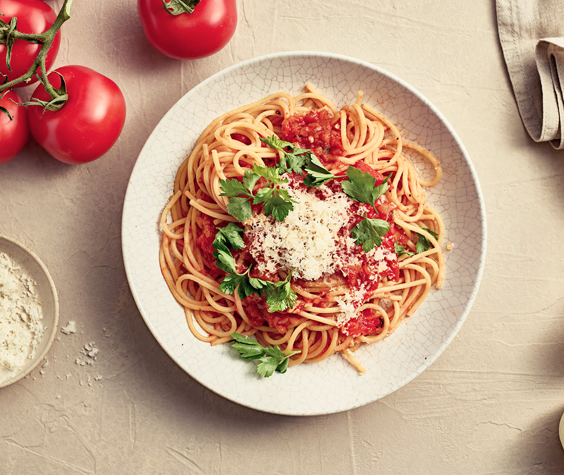 Pasta Pomodoro -annos lautasella. Ympärillä tomaatteja ja juustoraastetta.