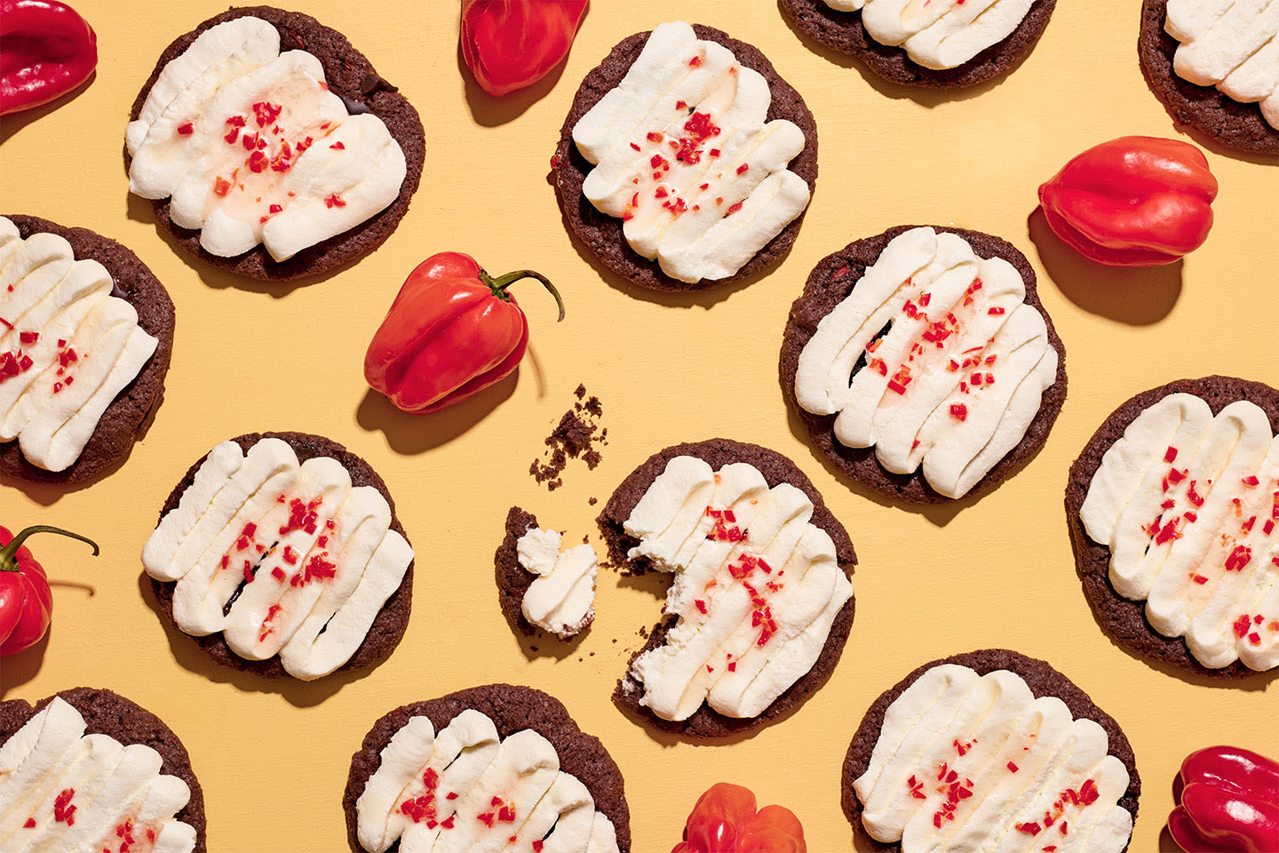 Herkullisia chilisuklaakeksejä valkoisella kuorrutteella ja punaisilla chilihiutaleilla keltaisella taustalla tuoreiden chilipaprikoiden kanssa.