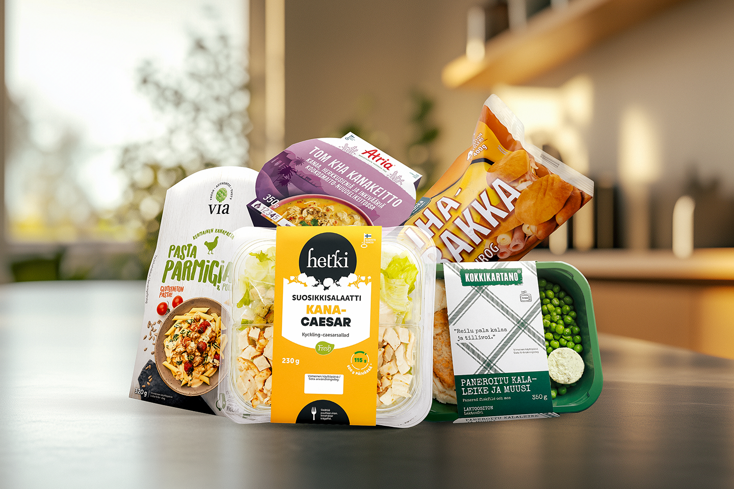 Hetki Kana Caesar -salaatti, Via Pasta Parmigiano, Kokkikartanon paneroitu kala ja muusi, Hoviruoka Lihapiirakka, Atria Tom Kha -kanakeitto keittiönpöydällä. 