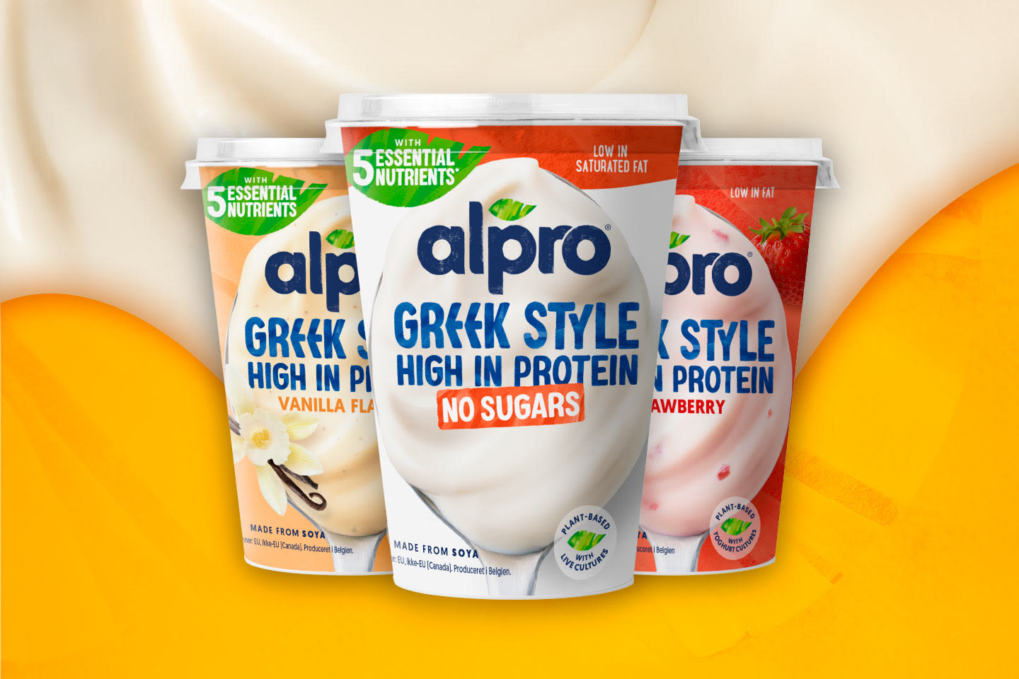 Kolme Alpro Greek Style -jogurttia rinnakkain: vanilja, sokeriton ja mansikka, oranssia taustaa vasten.